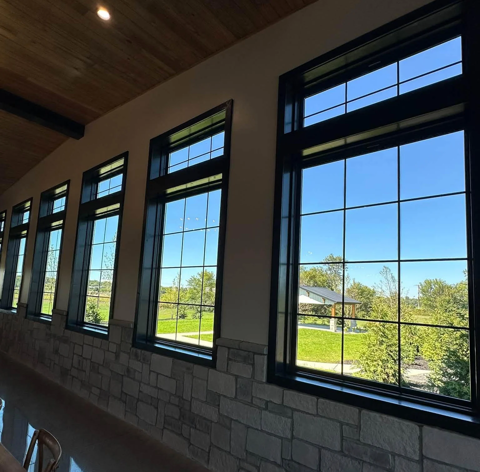 A row of tall black-framed windows inside a venue with timber ceilings and stone walls