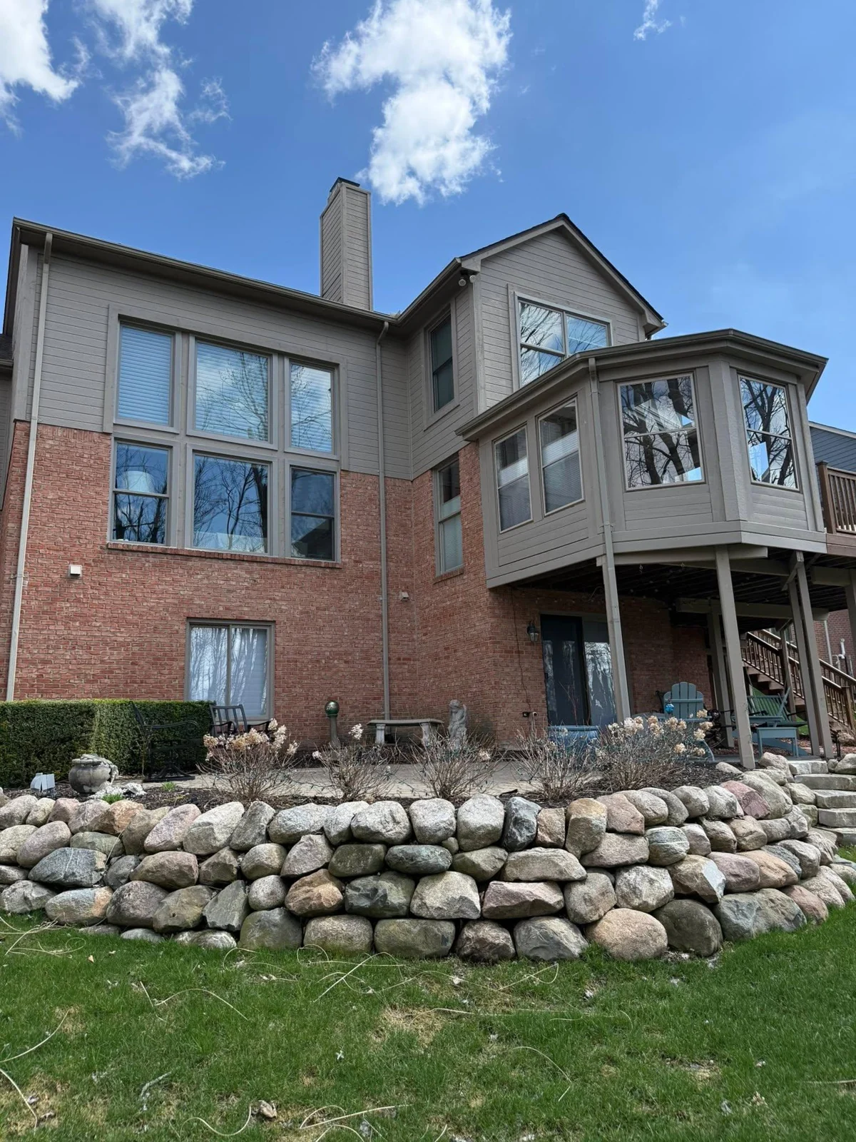 Rear elevation of a brick and siding home with large windows and a projecting bay window
