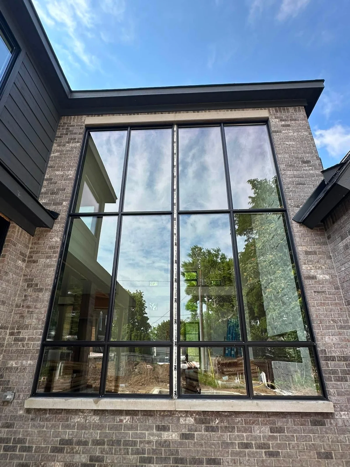 Two-story black-framed windows reflecting trees and blue sky on a brick home